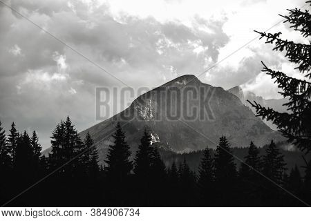 High Mountain In The Clouds Against The Background Of Trees, Black And White Epic Photo