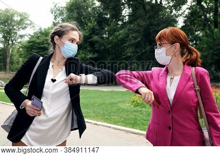 Young Businesswomans Wearing Medical Face Masks Greet Each Other Striking With Their Elbows. Meeting