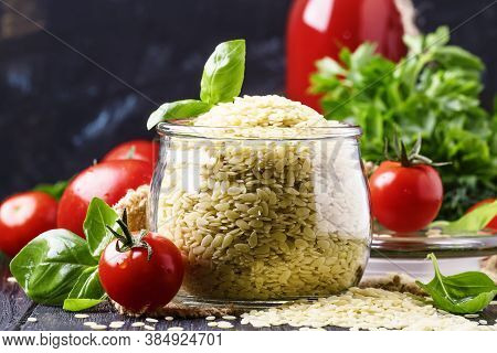 Italian Uncooked Pasta Riso Or Orzo In A Glass Jar, Tomatoes And Green Basil, Black Background, Sele