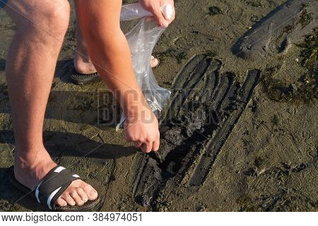 A Man Collects Therapeutic Mud On The Banks Of The Estuary In A Bag To Take With Him. Healing Mud Wi
