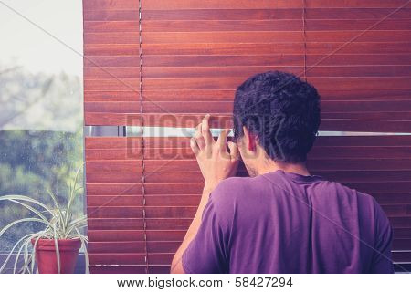 Young Man Peeping Out Through Venetian Blinds