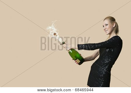 Beautiful young woman uncorking champagne bottle over colored background