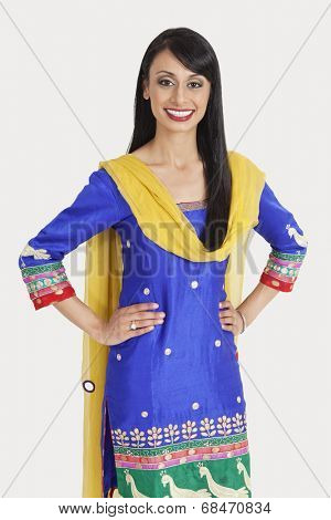 Portrait of pretty Indian woman in traditional wear standing with hands on hips over gray background