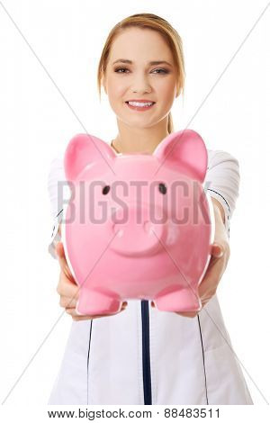 Young beautiful female doctor holding a piggybank.