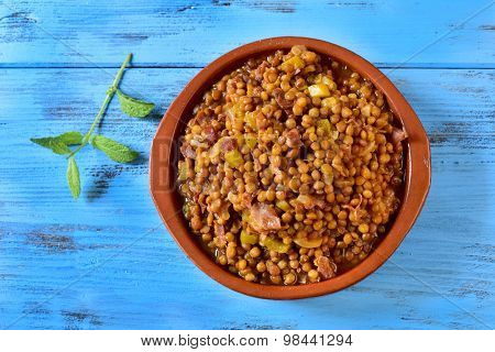 high-angle shot of an earthenware bowl with spanish lentil stew with serrano ham on a blue rustic wooden table