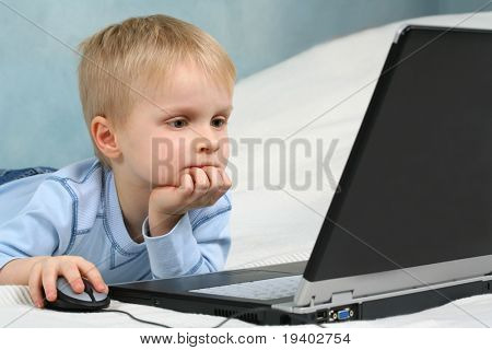 เด็ก preschool น่ารักตั้งอยู่บนนอน และเล่นกับคอมพิวเตอร์แล็ปท็อป