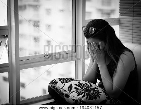 Woman Depressed or sad woman wear glasses sitting alone and covering her face due to having a head ache near the window.
