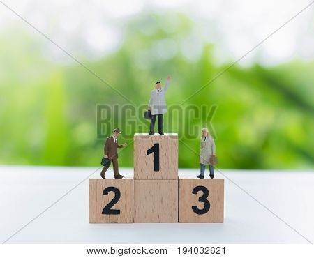 Miniature businessmans standing on a wooden winners podium with black number using as business leader victorie and achievement concept.