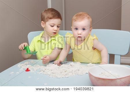 Group portrait of two cute siblings children playing kinetic sand or playdough together in kindergarden. Early creativity brain development concept. Lifestyle kids home activity.