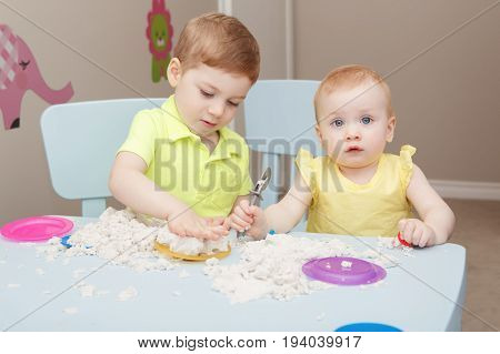 Group portrait of two cute siblings children playing kinetic sand or playdough together in kindergarden. Early creativity brain development concept. Lifestyle kids home activity.