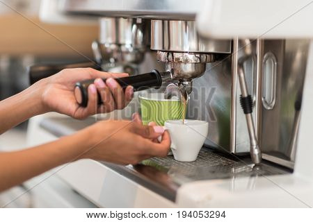 Cropped shot of female barista using coffee machine while making coffee in cafe