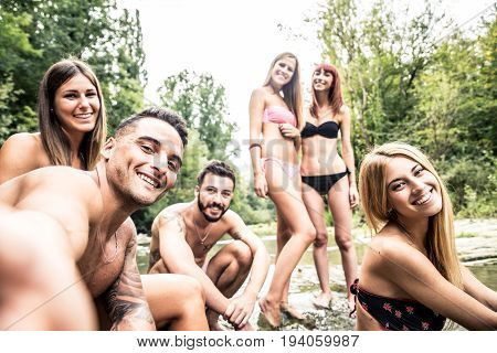Group of friends having fun at waterfalls in the nature - People sunbathing at a river during summertime vacation