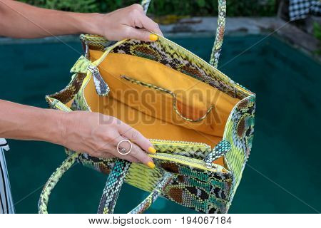 Fashionable woman holding luxury snakeskin python bag. Elegant outfit. Close up of purse in hands of stylish lady. Model posing near the swimming pool.