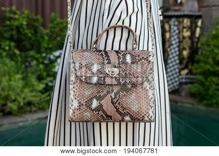 Fashionable woman holding luxury snakeskin python bag. Elegant outfit. Close up of purse in hands of stylish lady. Model posing near the swimming pool.