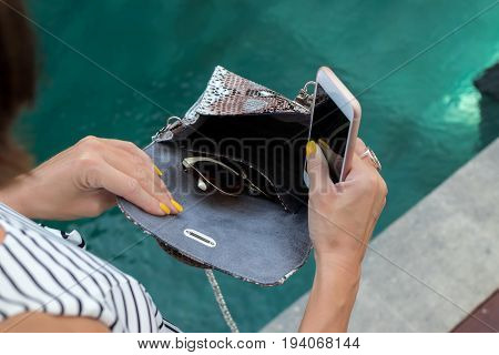 Fashionable woman holding luxury snakeskin python bag. Elegant outfit. Close up of purse in hands of stylish lady. Model posing near the swimming pool.