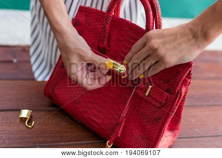 Fashionable woman holding luxury snakeskin python bag. Elegant outfit. Close up of purse in hands of stylish lady. Model posing near the swimming pool.