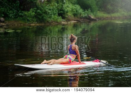Young Woman Doing Fitness On A Board With An Oar. Side View - The Concept Of Harmony With Nature, A