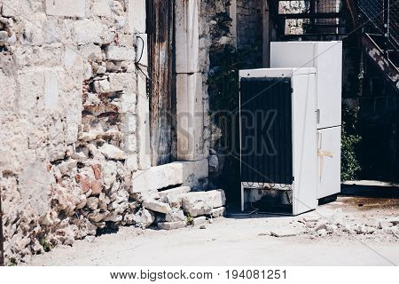 Old broken refrigerators in the yard of an old ruined house. Electro waste
