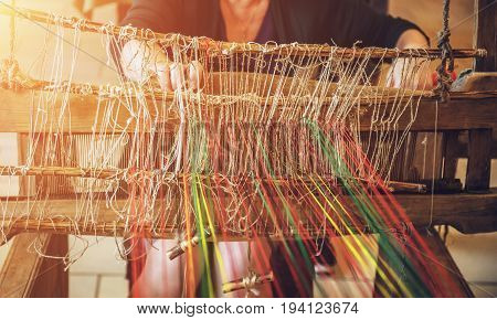 Craftsperson Woman working behind an old wooden loom in the sunlight in workshop