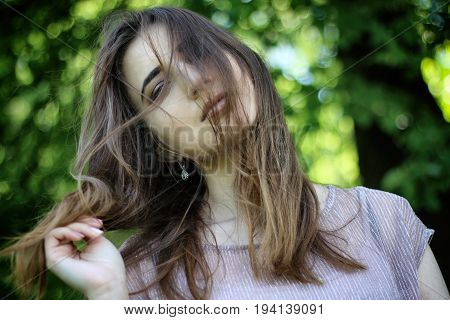 Portrait of a young beautiful woman with a hairstyle on the face in the Park. Windy day. Background Bokeh