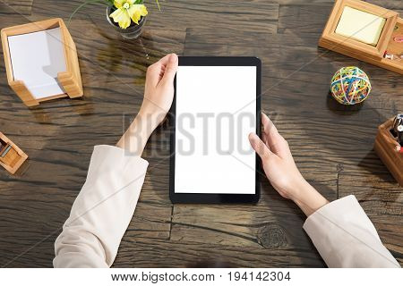 Close-up Of A Businessperson Holding Blank Digital Tablet Over The Wooden Desk