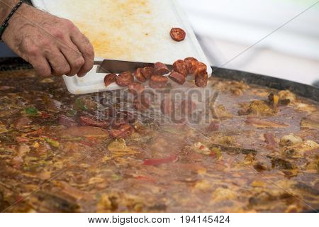 Cooker putting chorizo sausage pepperoni in paella jumbalaya louisiana country plate