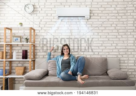 Happy Young Woman Holding Remote Control Relaxing Under The Air Conditioner