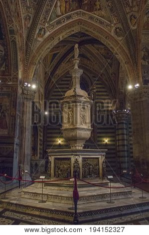 Italy Siena - December 26 2016: the view of font in Siena Baptistery with marble tabernacle and statue by Jacopo della Quercia panel by Ghiberti and Faith by Donatello on December 26 2016 in Siena Tuscany Italy.