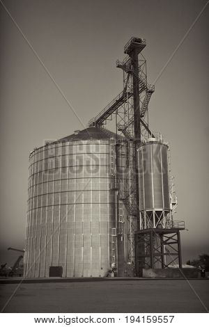 newly constructed metal grain silo and elevator against clear sky, black and white, sepia toned image