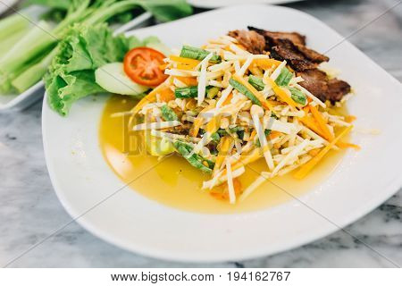Papaya Salad with Grilled Pork Neck on white plant.