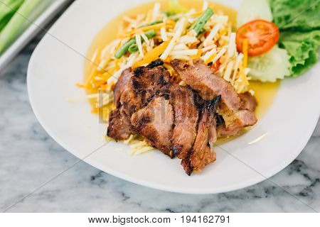 Somtum roasted pork neckon a white plate , Thai food.
