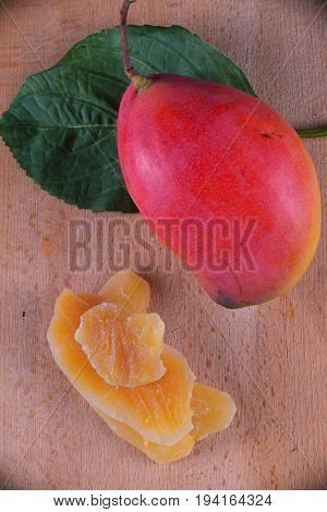 Detail of dried mango slices with whole ripe fruit on wooden background