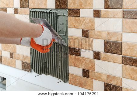 A tile's hand is holding a notched trowel and combing a adhesive for installation a tile.