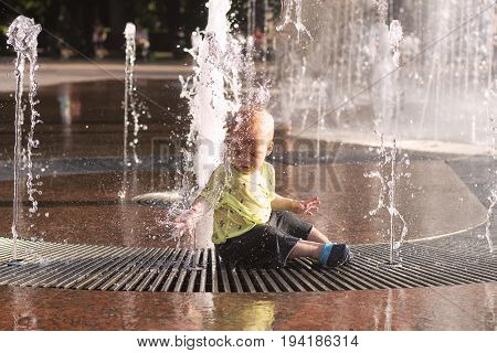 Cute Toddler Sitting In Fountain. Awesome Baby Boy Having Fun And Plaing In Fountain.