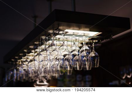 Empty wine glasses hanging upsidedown in bar interior. Classic wineglasses hanger on restaurant or pub background