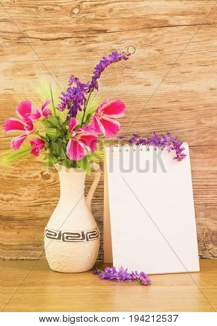 Mocap, background from a blank white sheet of paper in a notebook near bright plastic walls and ceramic vase with pink and purple garden flowers on wooden table, vertical, mock up