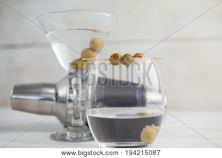 Close up of green olives in vodka martini with cocktail shaker on wooden table