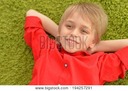 Portrat of blonde little boy lying on green carpet in room