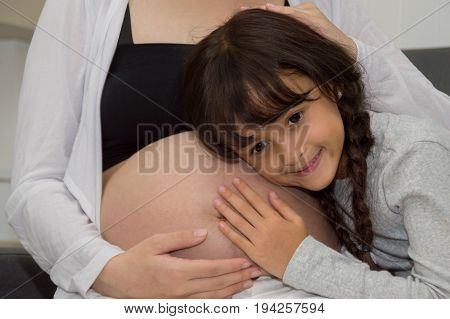 The girl is listening to belly of pregnant mother