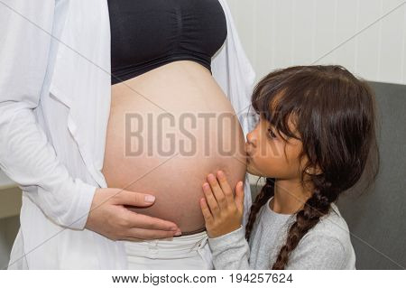The girl is listening to belly of pregnant mother