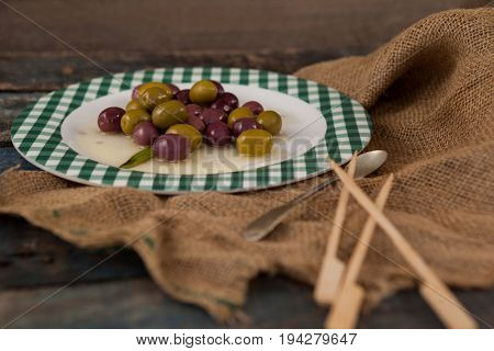 Close up of green and black olives served in plate on wooden table