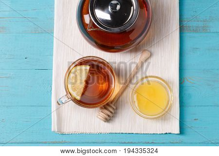 Glass cup of tea with lemon, glass teapot and honey on blue wooden table.