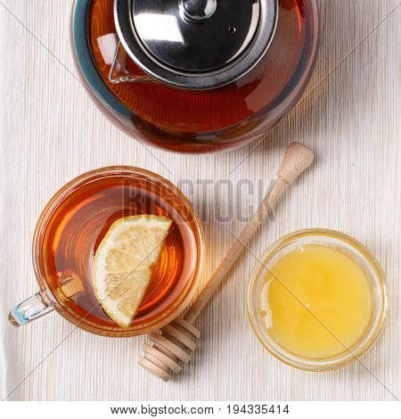 Glass cup of tea with lemon, glass teapot and honey on blue wooden table.