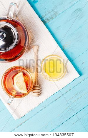 Glass cup of tea with lemon, glass teapot and honey on blue wooden table.
