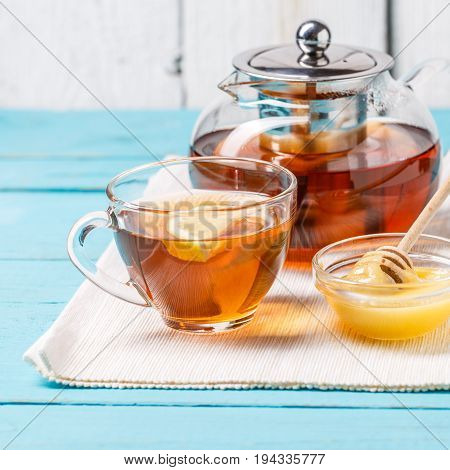 Glass cup of tea with lemon, glass teapot and honey on blue wooden table.