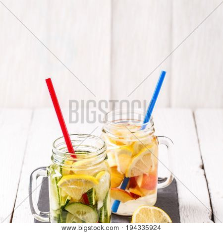 Two mugs of infused detox diet refreshing waters - first with cucumber and lemon, second with lemon and peach on white wooden table