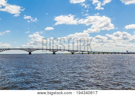 Road bridge across the Volga river between the cities of Saratov and Engels, Russia. Summer river landscape. Blue sky, white clouds.