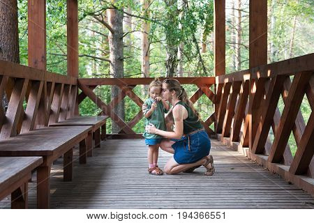 Mother and daughter in a wooden summerhouse. Daughter is holding a flower, mothers is hugging her.