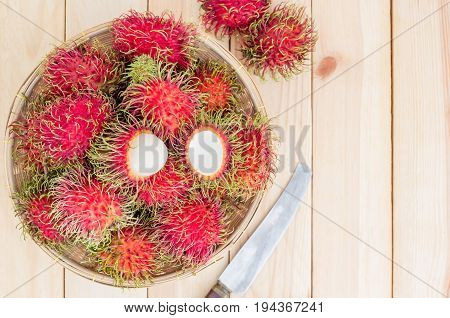 fresh tropical rambutan fruits over basket with knife on wood background Top view with copy space and text.