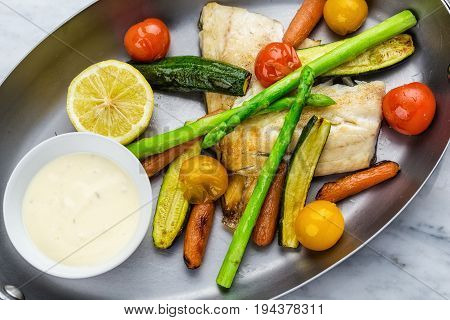 Grilled fish and vegetables with sauce served in metalic bowl on marble serface